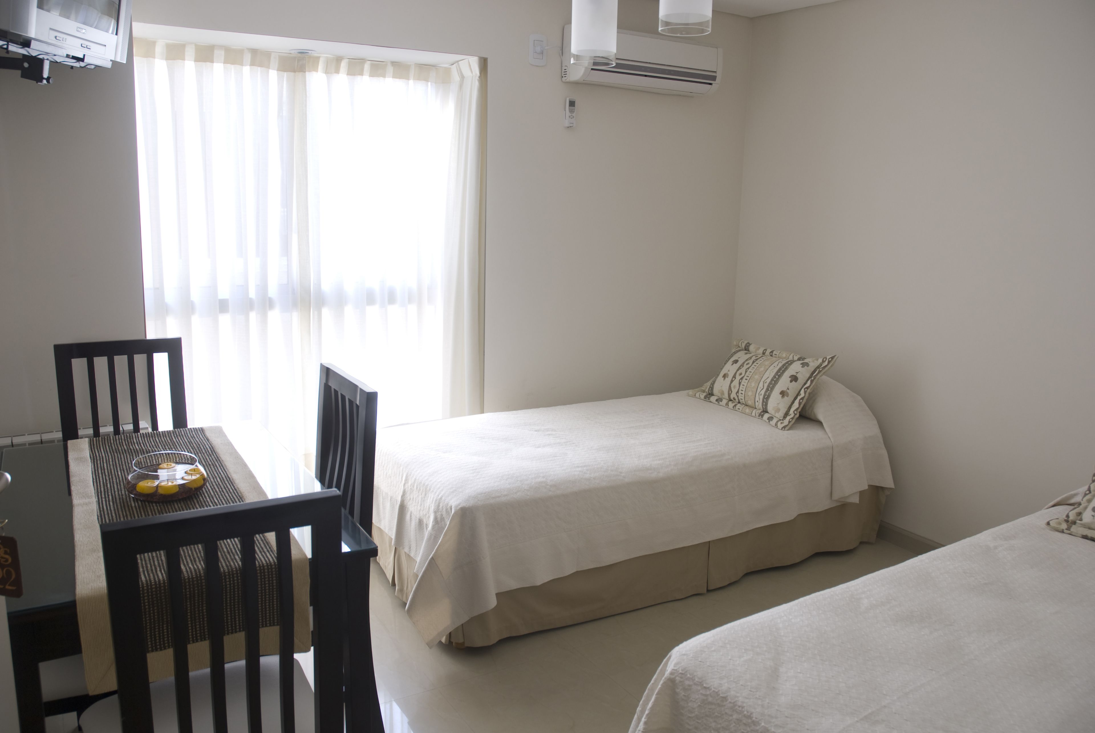 A small, clean room with a single bed, a chair, a table, and a window with curtains.