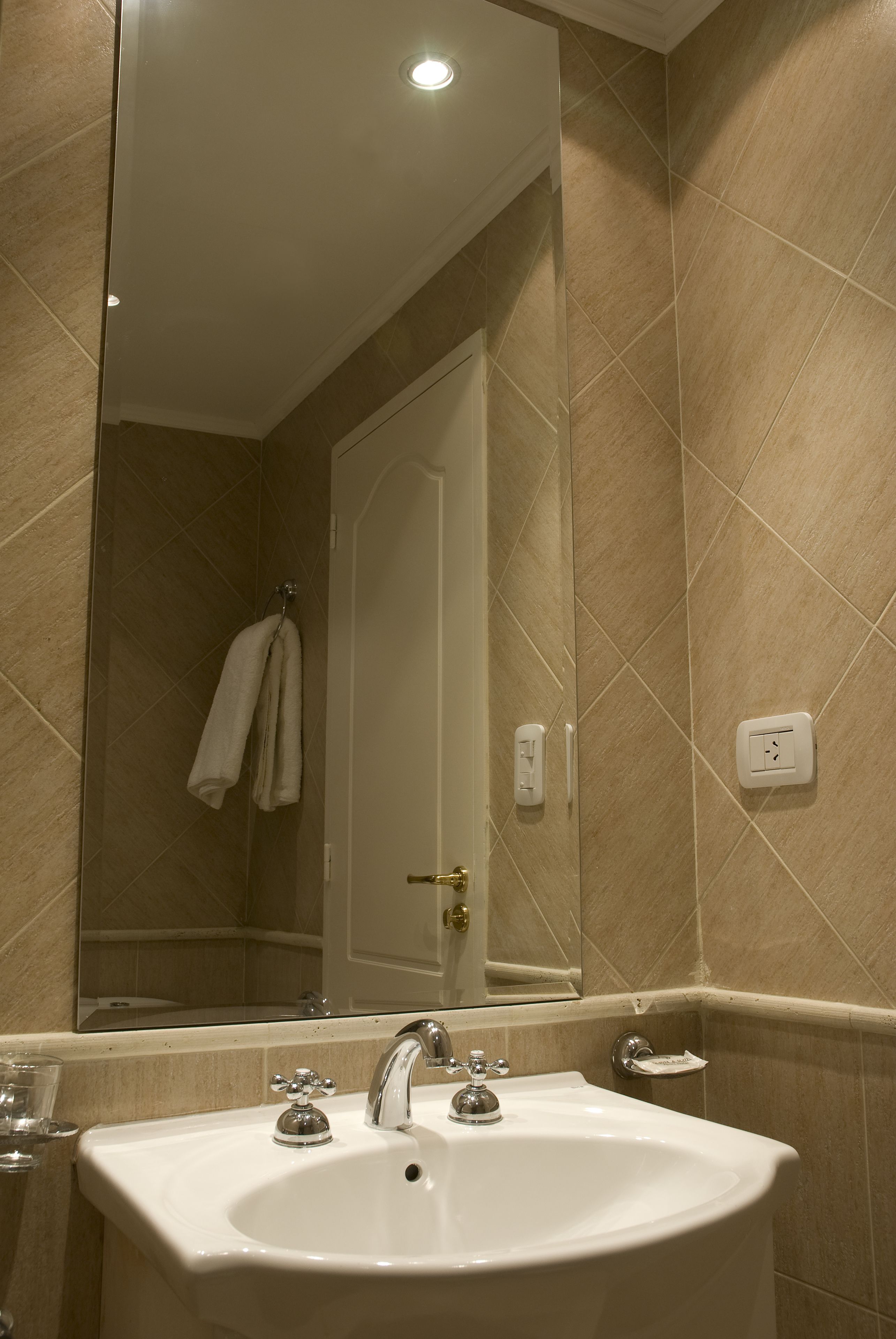 Un baño con lavamanos blanco, espejo y paredes con azulejos color beige.