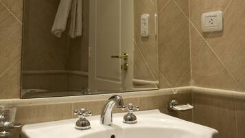 Un baño con lavamanos blanco, espejo y paredes con azulejos color beige.