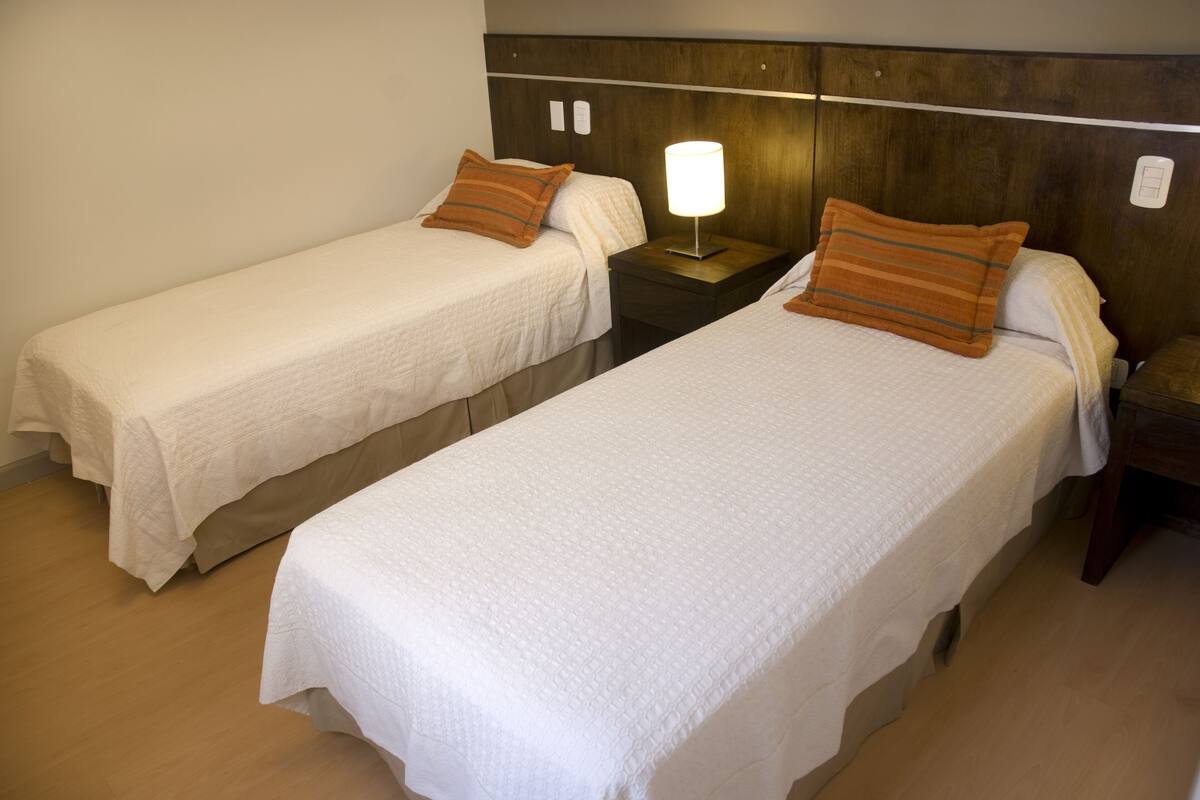Two single beds with white bedding and wooden headboards in a hotel room.