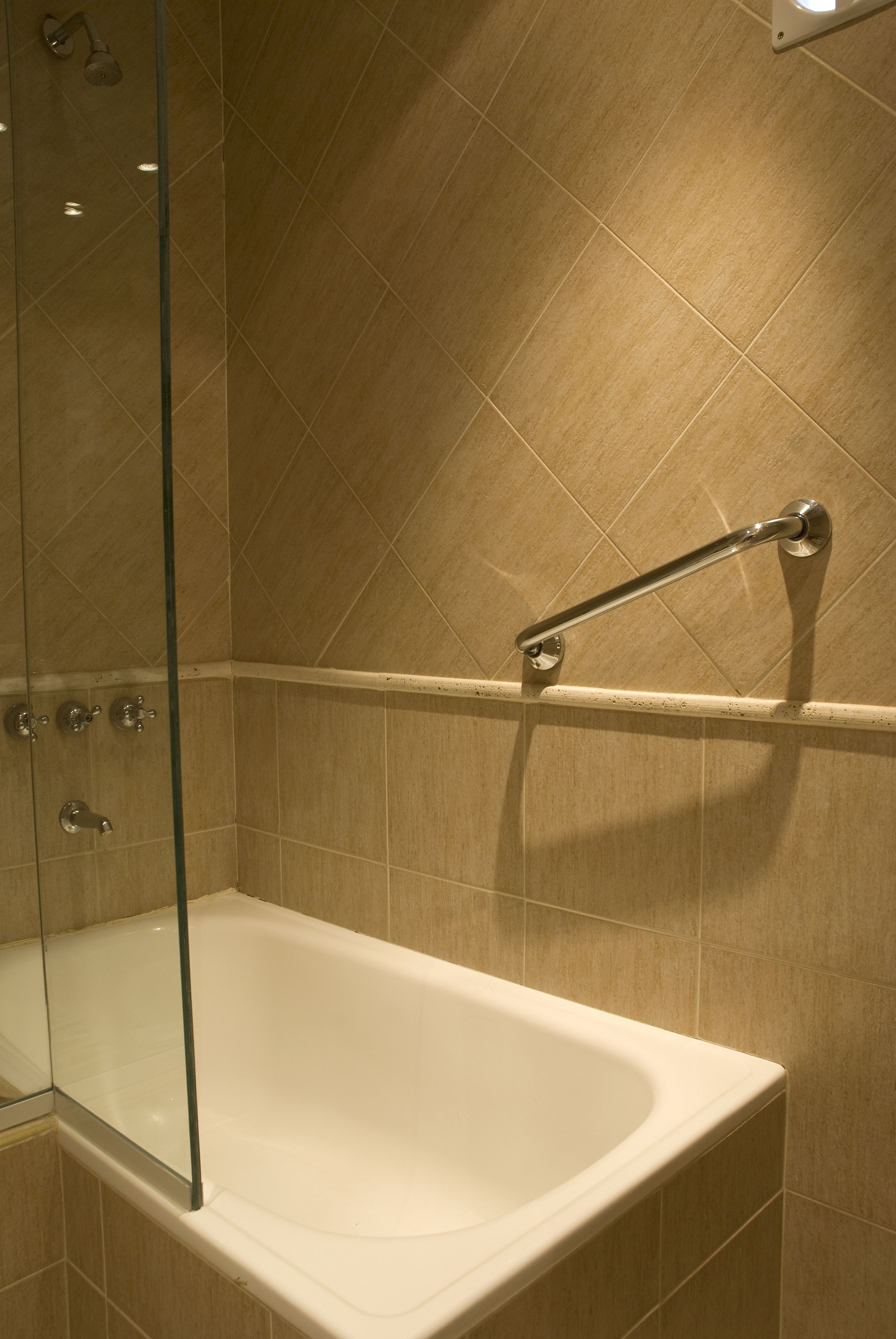 Baño con bañera, cabina de ducha de vidrio y barra de apoyo.