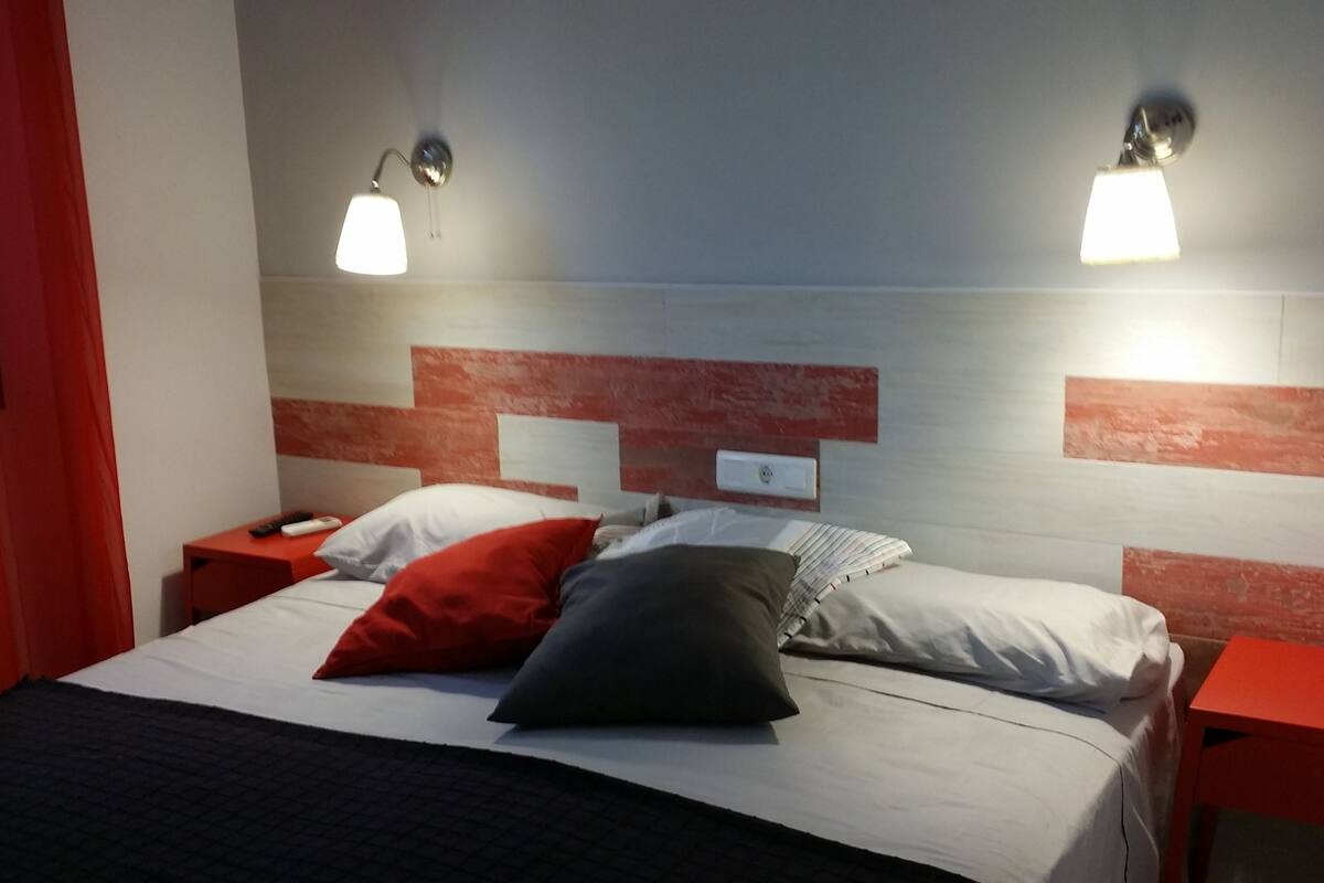 Ein Hotelzimmer mit einem Bett, zwei Nachttischen, einem roten Vorhang und zwei Wandlampen.