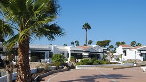 Un complexe hôtelier avec des bâtiments blancs, des palmiers et une terrasse carrelée.