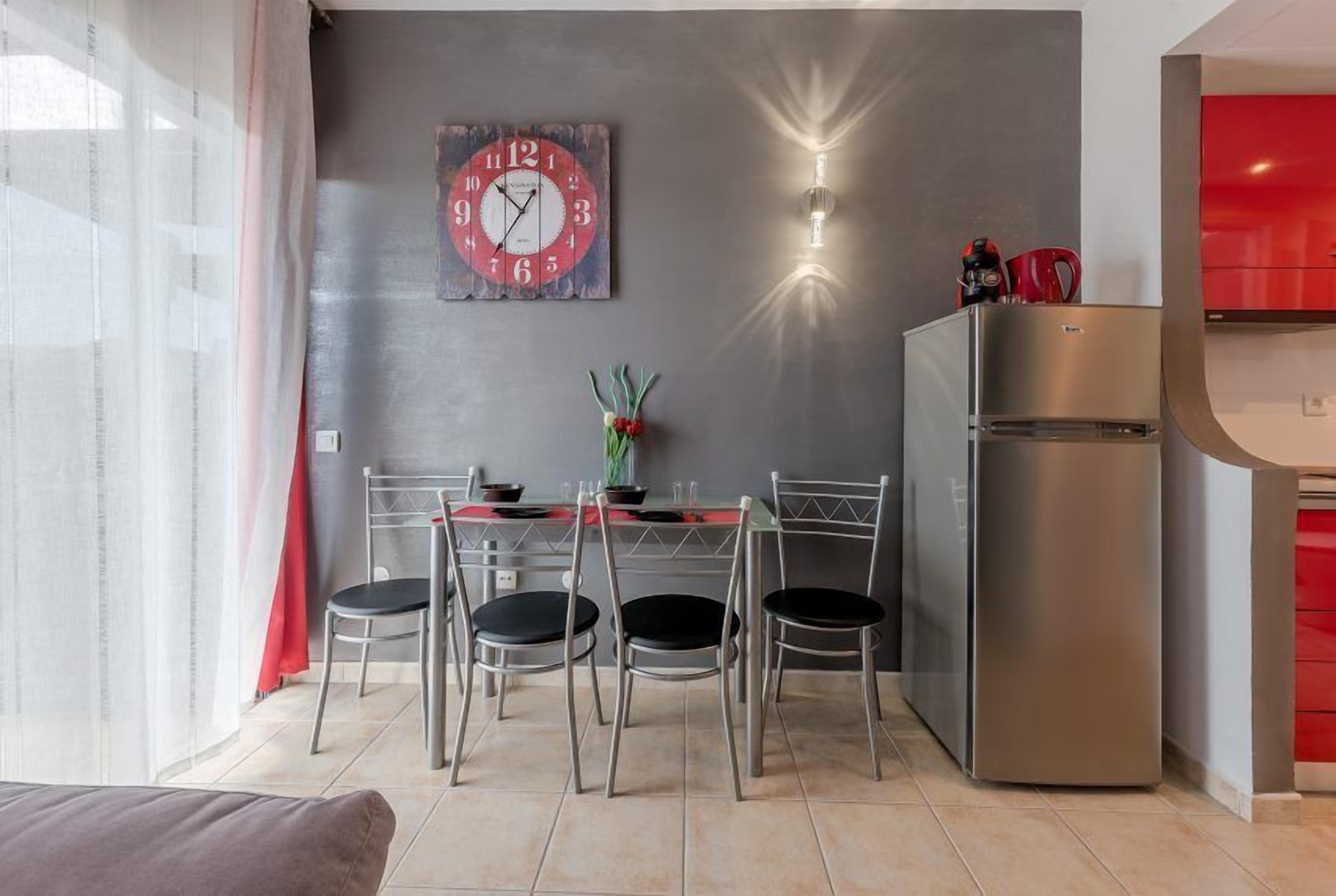 Una cocina moderna con un refrigerador de acero inoxidable, un reloj en la pared y un comedor con mesa y sillas.