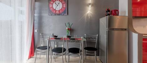 Una cocina moderna con un refrigerador de acero inoxidable, un reloj en la pared y un comedor con mesa y sillas.