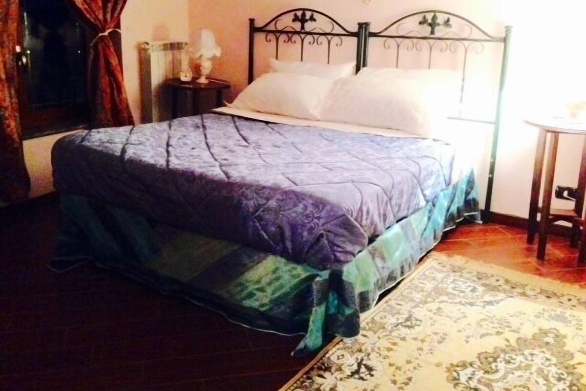 A bedroom with a bed, a nightstand, a lamp, and a window with curtains.