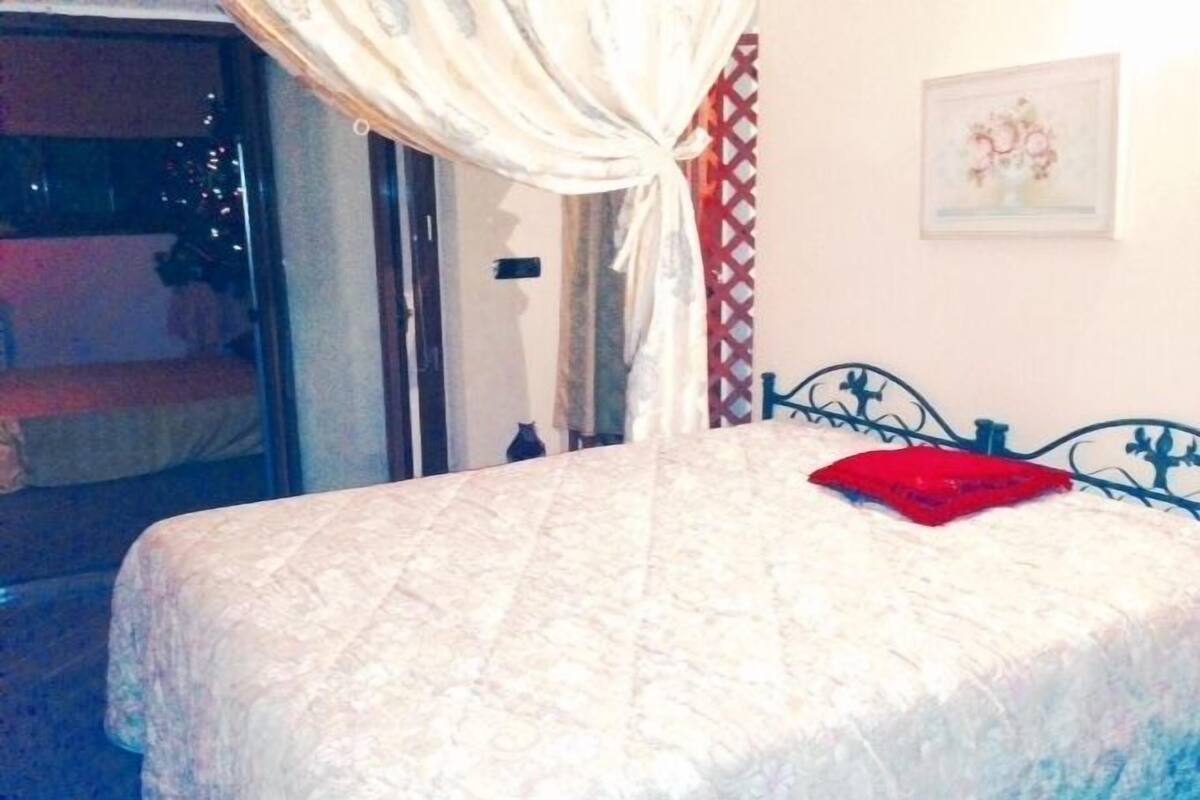 A bed with a white bedspread and a red pillow, a metal headboard, and a window with curtains.