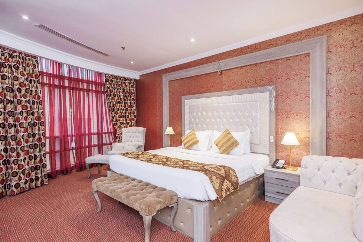 A spacious bedroom with a large bed, a bedside table with a lamp, a chair, and a bench.