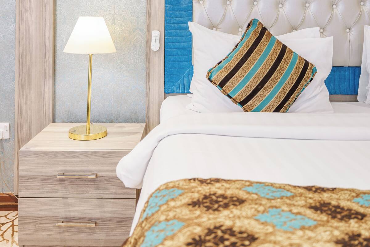 A bedroom with a tufted headboard, a bedside table with a lamp, and a patterned bedspread.