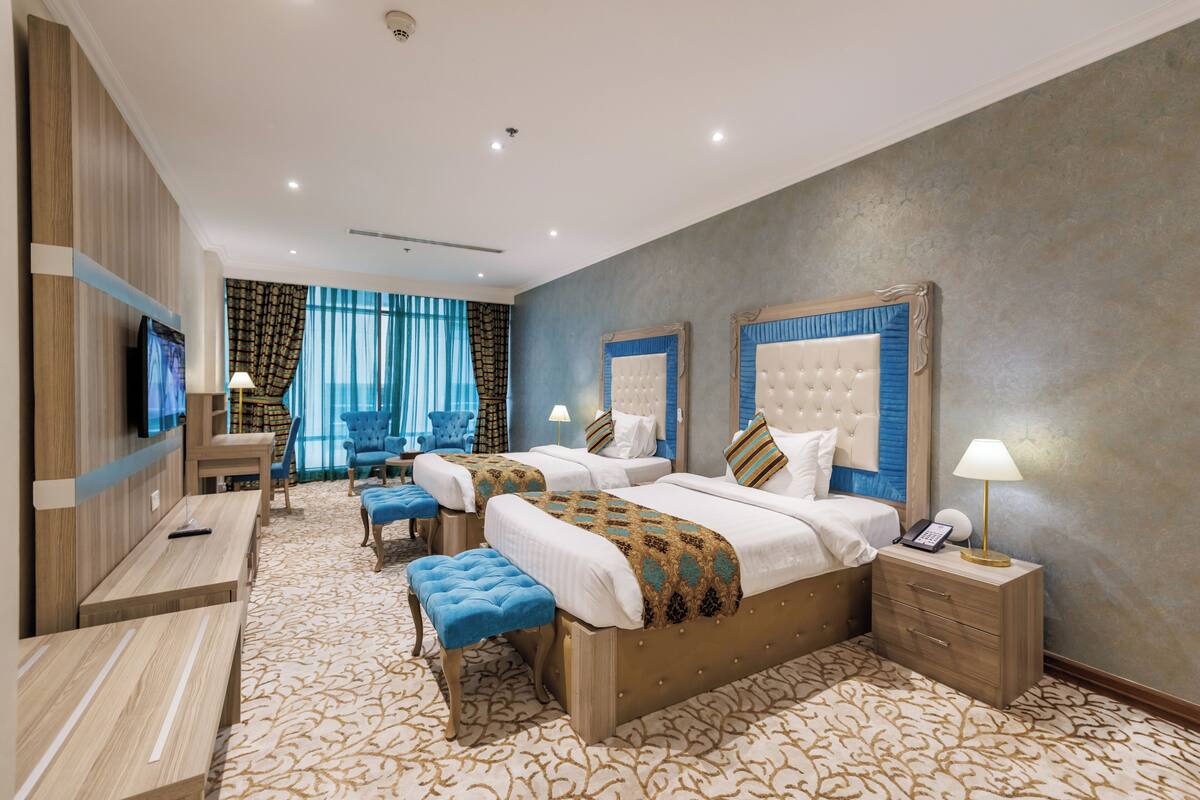 A hotel room with two beds, a TV, a desk, and a chair.