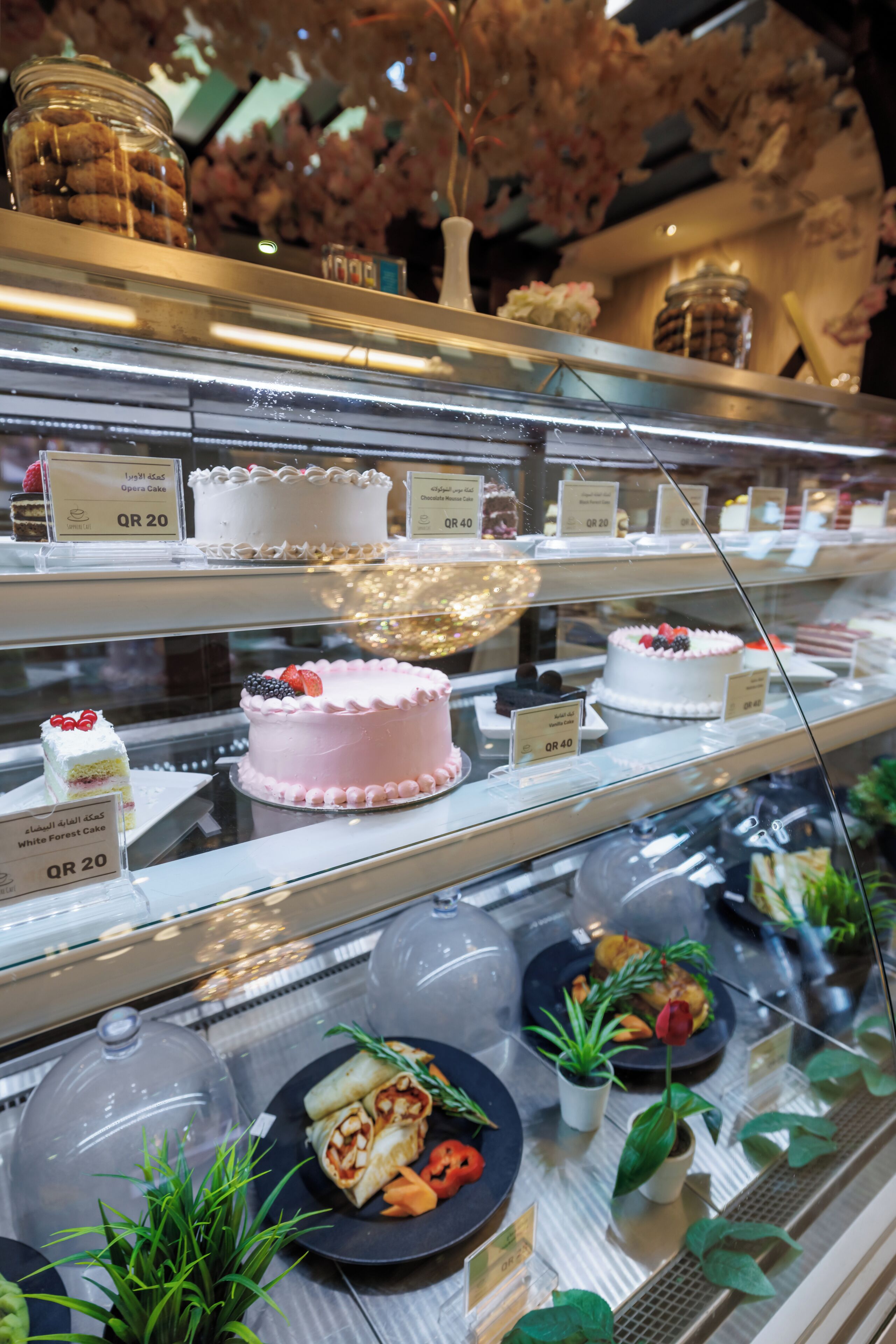 A bakery display case with various cakes and pastries, including a white cake and a pink cake with berries.
