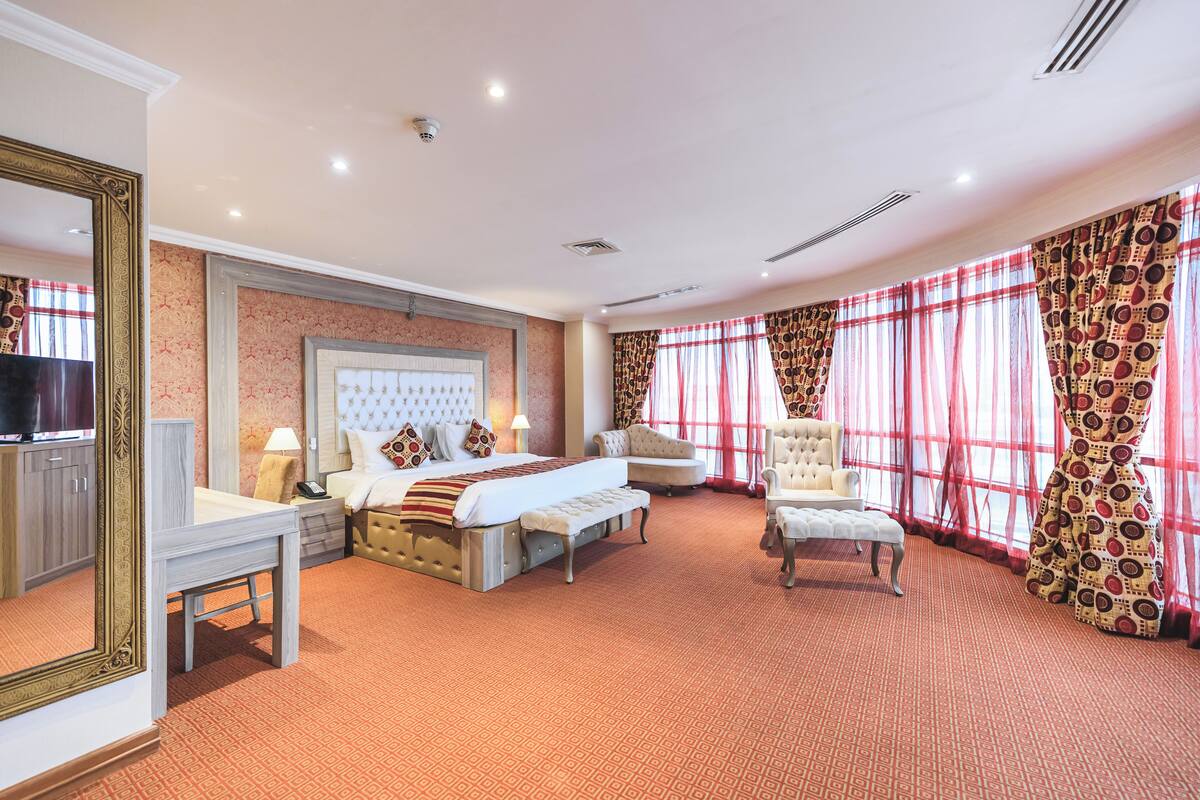 A spacious hotel room with a large bed, a sofa, a chair, and a desk.