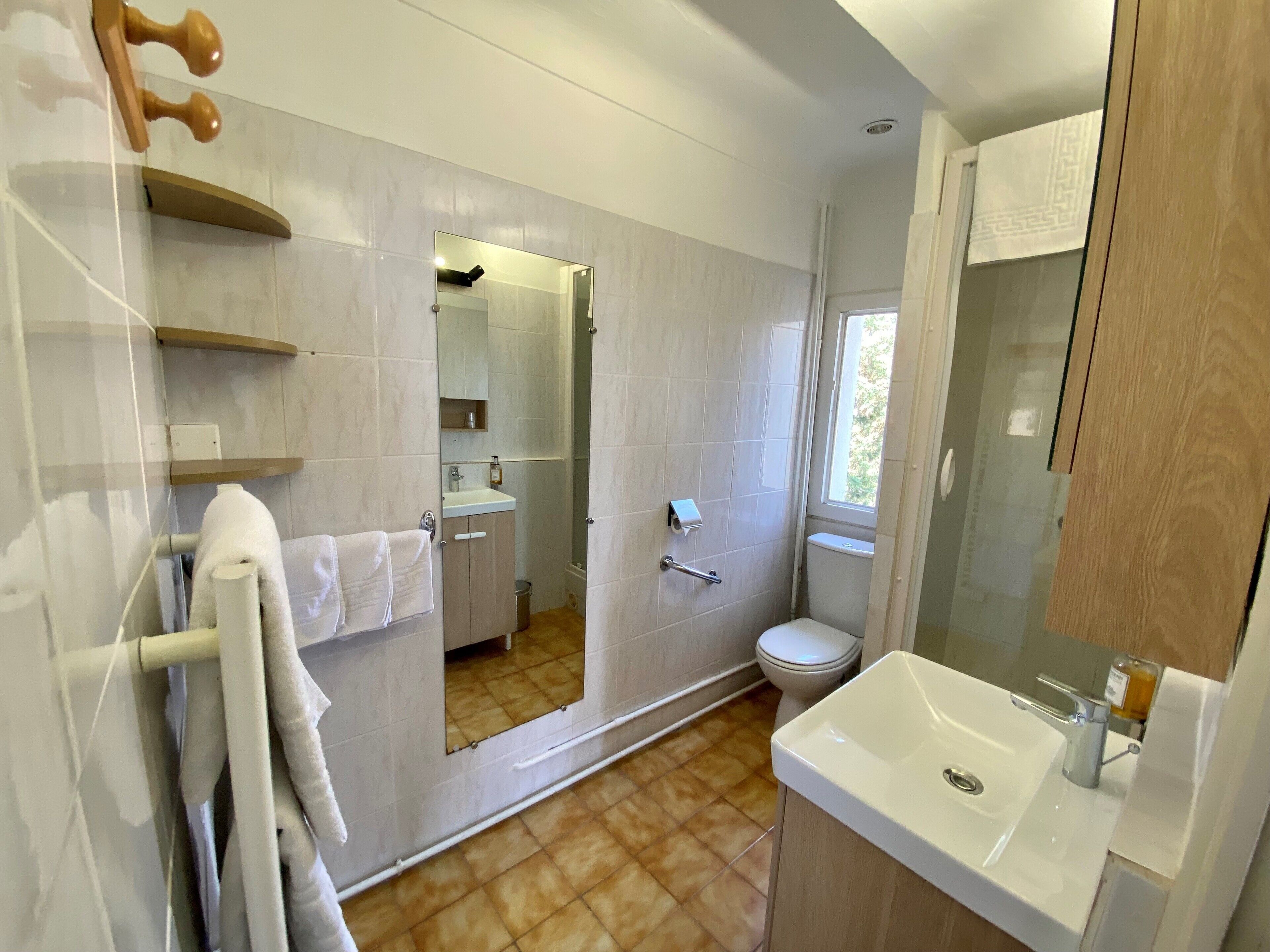 Une salle de bain moderne avec un grand miroir, un lavabo et des toilettes. On y trouve un porte-serviettes sur lequel est accrochée une serviette blanche.