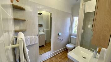 Une salle de bain moderne avec un grand miroir, un lavabo et des toilettes. On y trouve un porte-serviettes sur lequel est accrochée une serviette blanche.