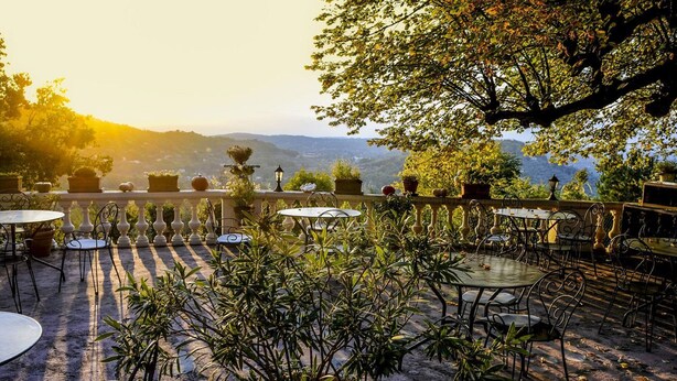 An outdoor patio with round tables and chairs, surrounded by potted plants and a view of distant hills. - Logis hôtel la Bellaudière (Grasse)