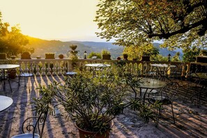 An outdoor patio with round tables and chairs, surrounded by potted plants and a view of distant hills. - Logis hôtel la Bellaudière (Grasse)
