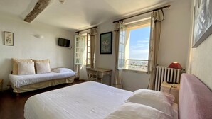 A bedroom with a large bed, a desk, a chair, and a radiator. - Logis hôtel la Bellaudière (Grasse)