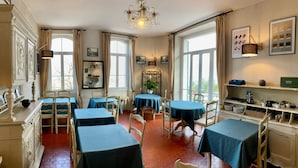 A dining area with hexagonal patterned floor tiles, multiple tables with blue tablecloths, and a chandelier. - Logis hôtel la Bellaudière (Grasse)