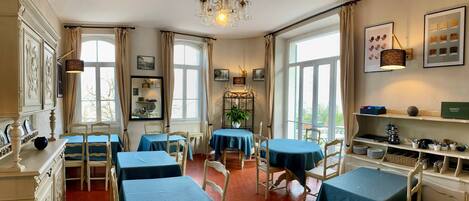 A dining area with hexagonal patterned floor tiles, multiple tables with blue tablecloths, and a chandelier.