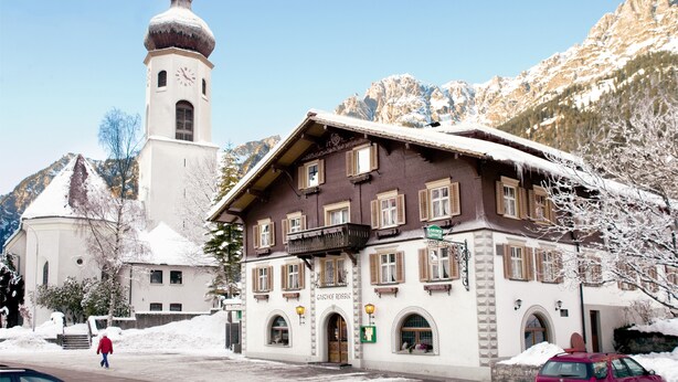 Ein Gebäude mit einem Glockenturm und einem mit Schnee bedeckten Dach, umgeben von Bergen.