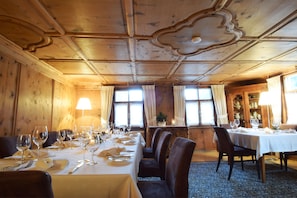 A dining area with wooden walls and ceiling, tables set for dining, and large windows with curtains.