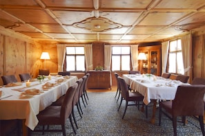 A dining room with wooden paneling, large windows with curtains, and tables set for a meal.