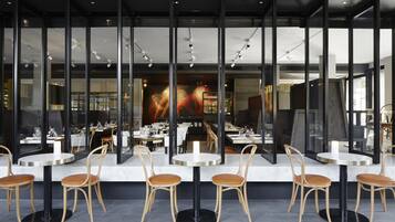 Een restaurant met ronde tafels en houten stoelen, grote ramen en een modern interieur.