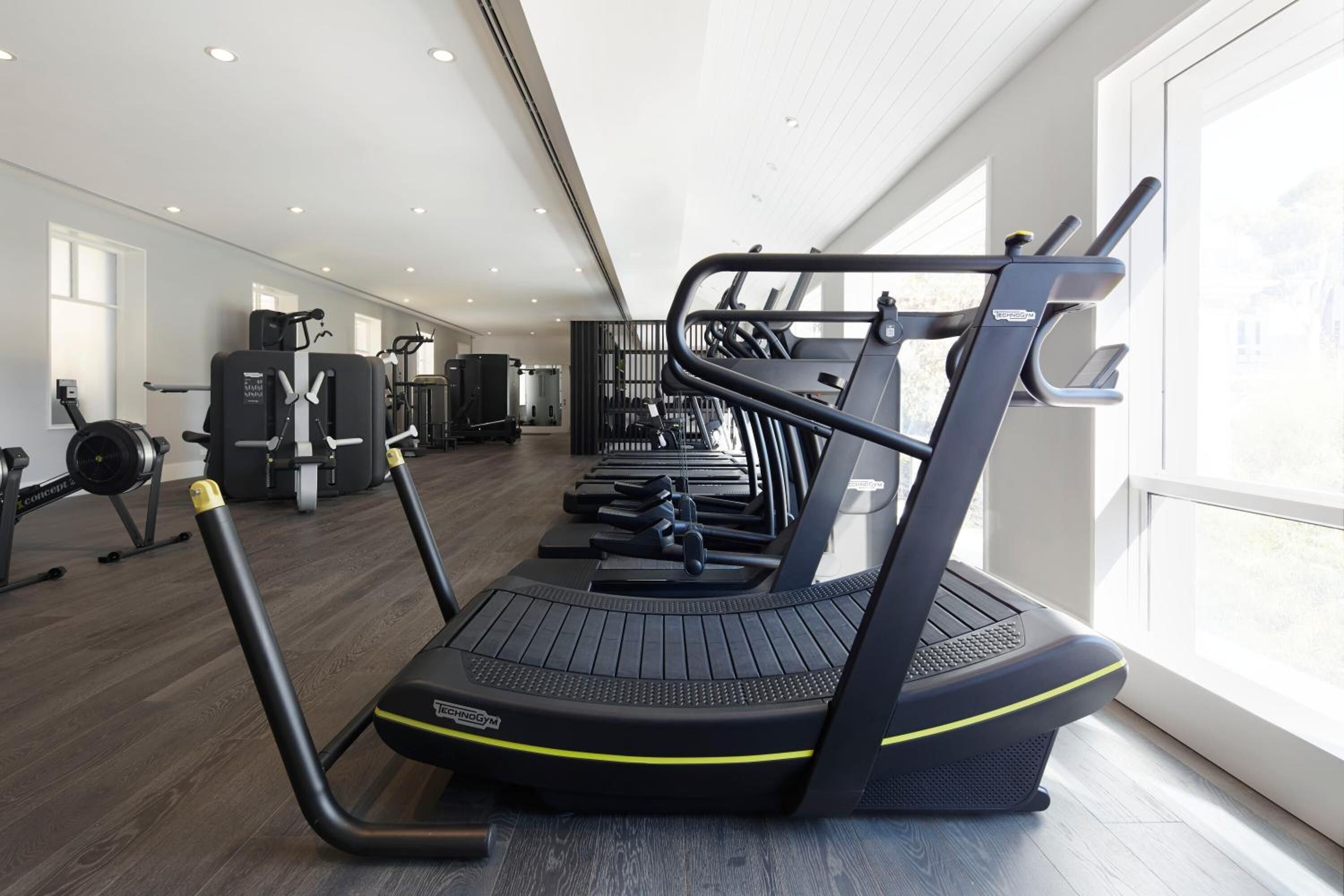 A gym with treadmills, weight machines, and a large window providing natural light.