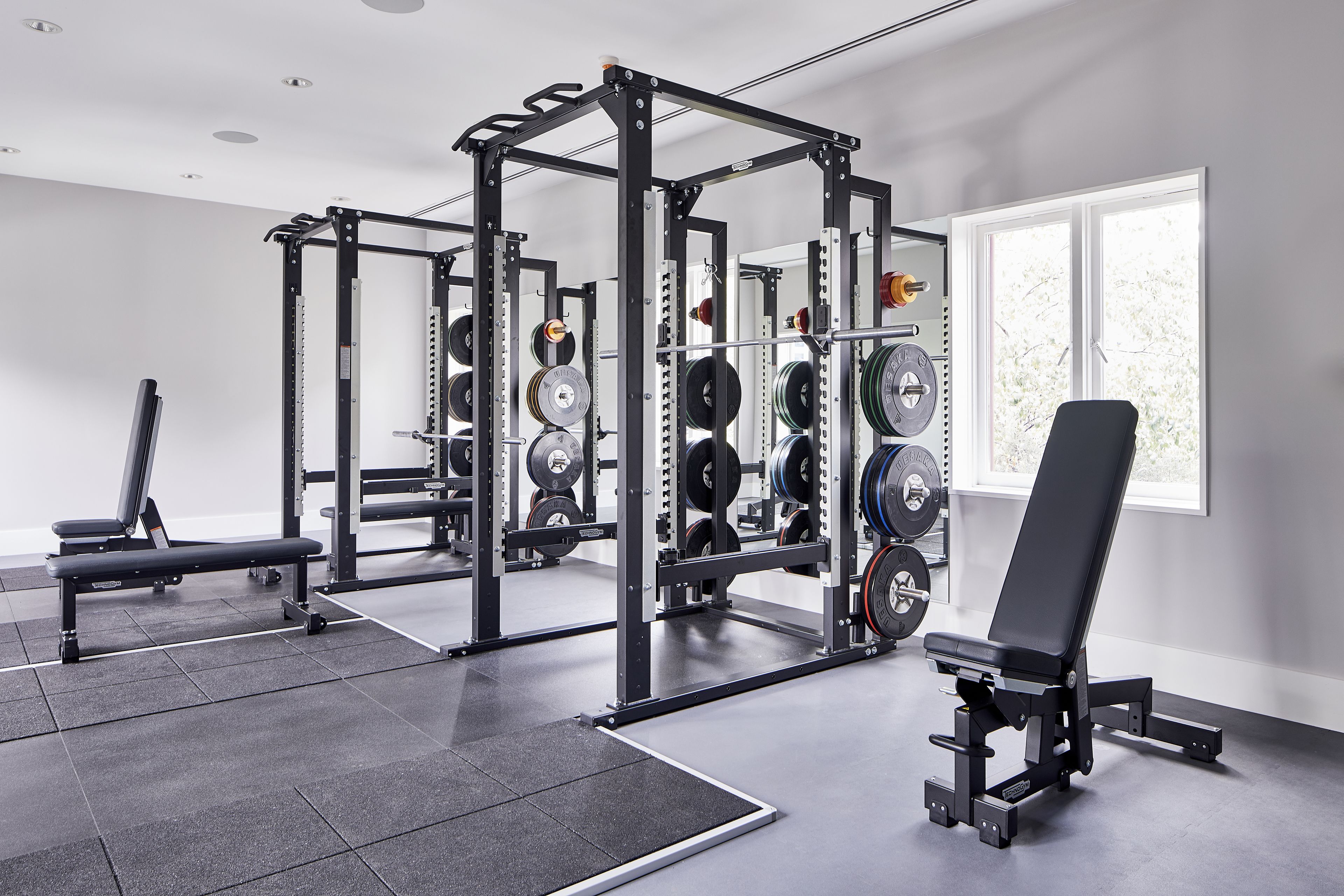 A gym with weightlifting equipment, a bench, and a window with natural light.
