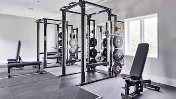 A gym with weightlifting equipment, a bench, and a window with natural light.