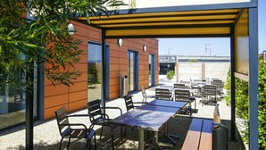 Un patio al aire libre con mesas y sillas, un edificio de fachada marrón y un cielo despejado.