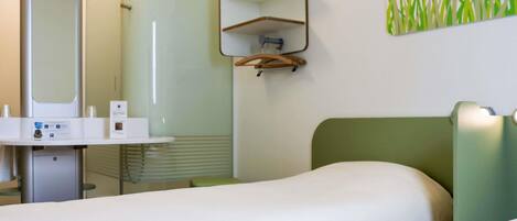 Habitación de hotel con cama, mesita de noche, espejo, estante y una obra de arte colgada en la pared.