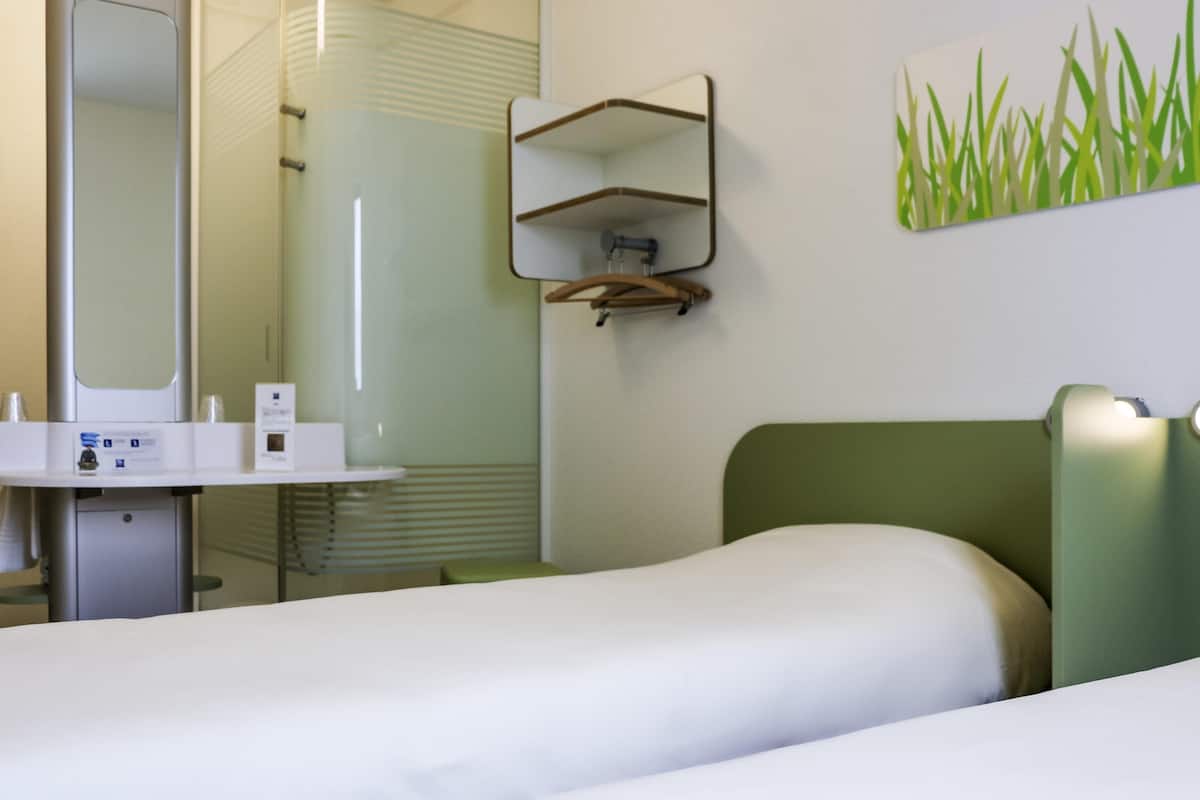 Habitación de hotel con cama, mesita de noche, espejo, estante en la pared y un cuadro de hierba.