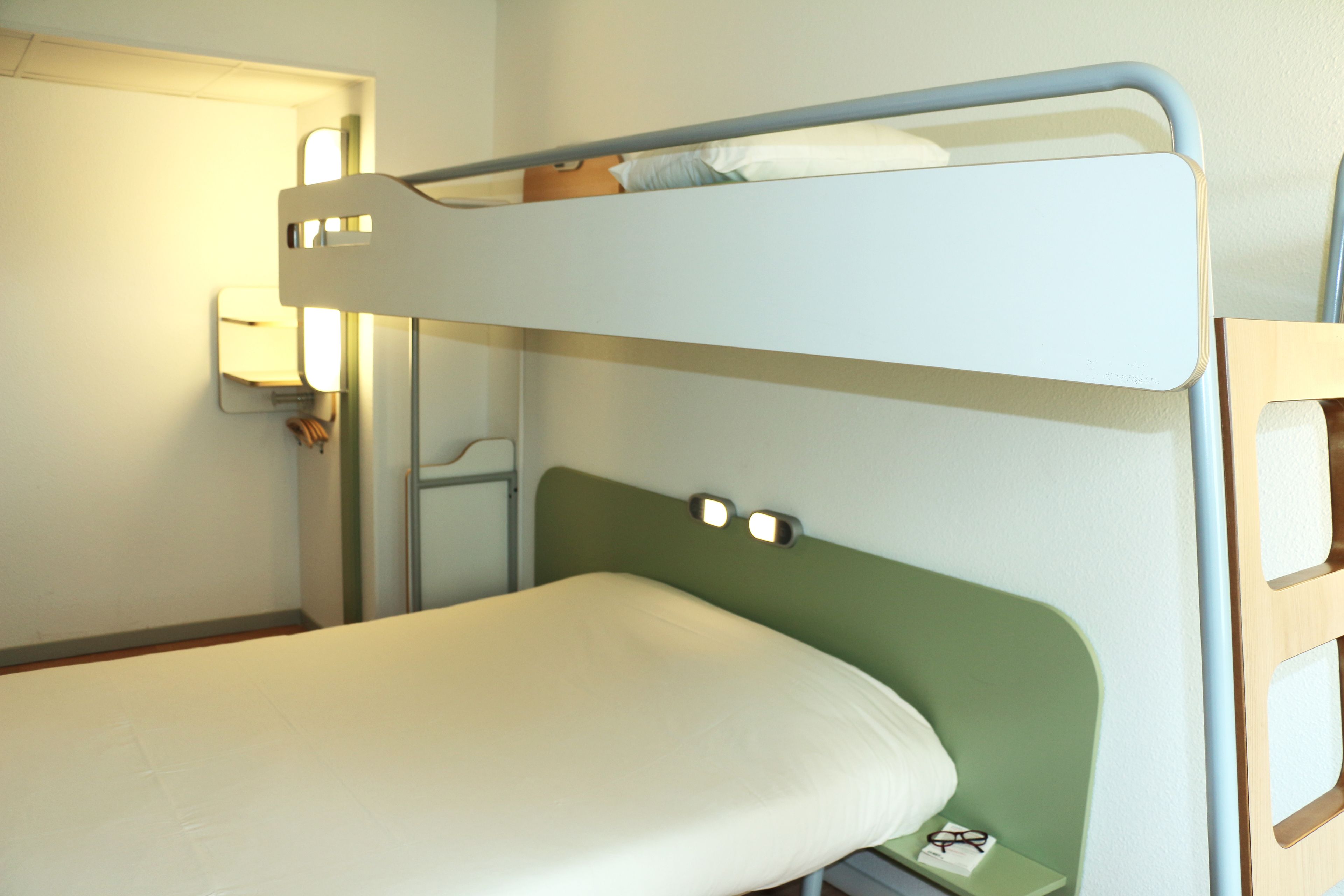 Un lit superposé avec une tête de lit verte et un matelas blanc.