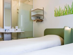 A hotel room with a bed, a bedside table, a mirror, a shelf, and a wall-mounted artwork. - Ibis Budget Castelnaudary (Castelnaudary)