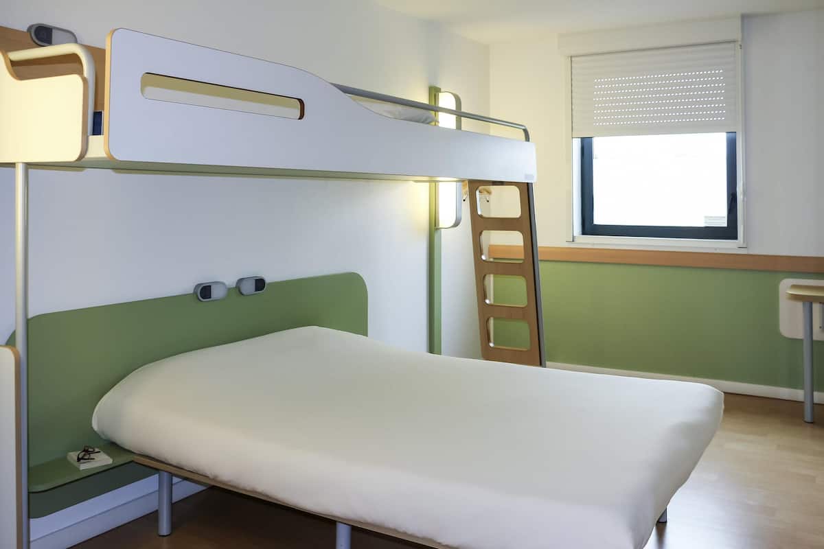 A bunk bed with a desk and ladder, a window with blinds, and a green wall.