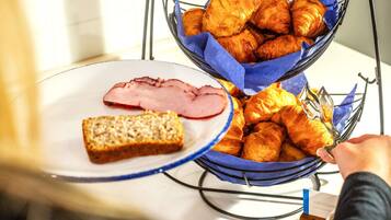Un bufé de desayuno con croissants, jamón y una rebanada de pan en un plato.