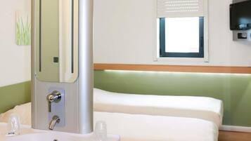 A hotel room with a bed, a sink, a mirror, a window with blinds, and a television mounted on the wall.
