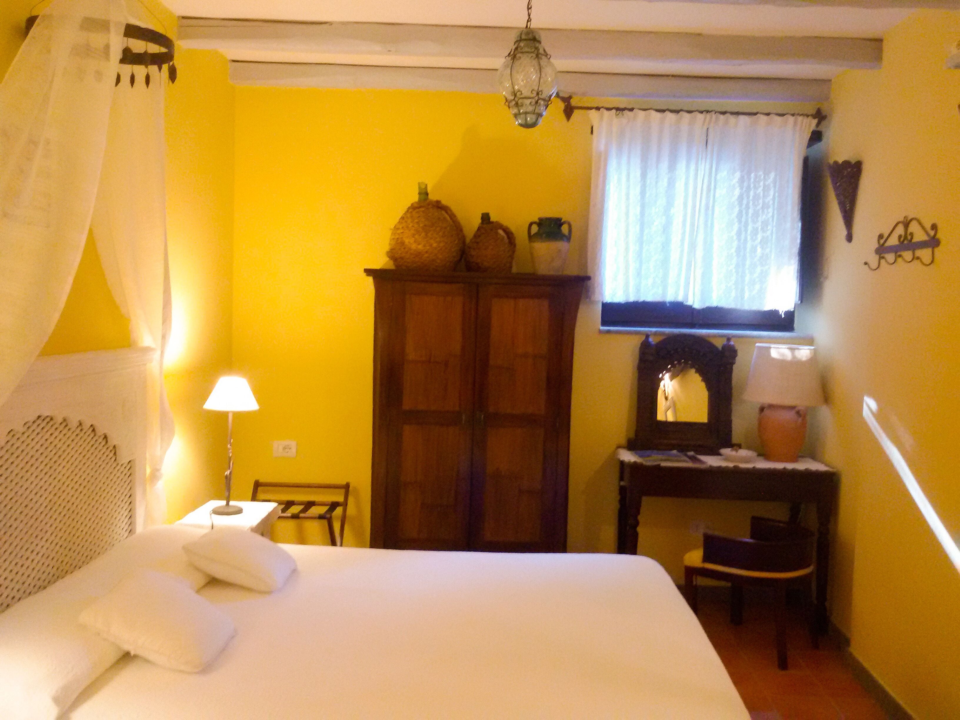 A bedroom with a bed, a wooden wardrobe, a table with a lamp, and a window with curtains.