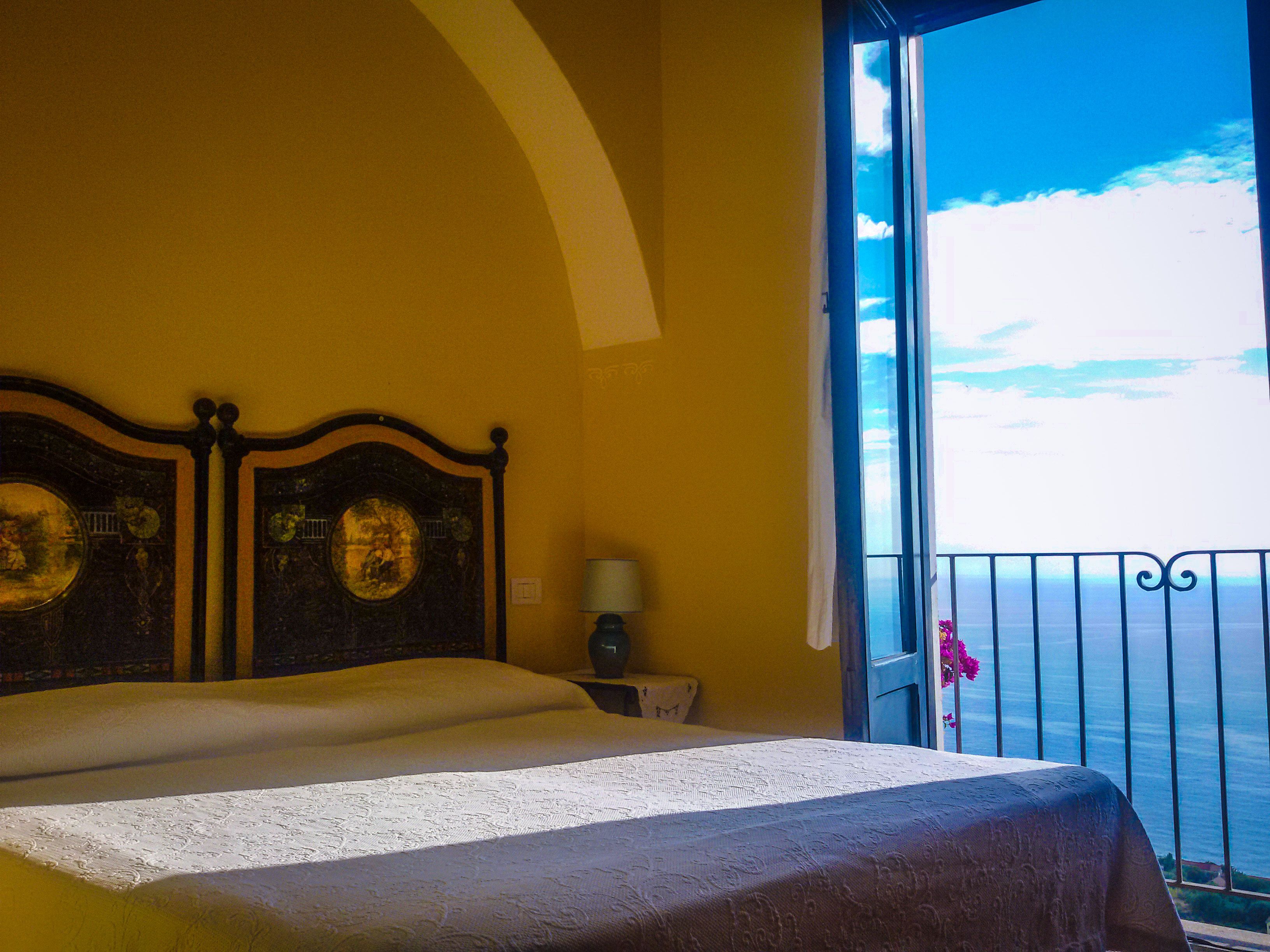 Un dormitorio con una cama grande, una mesita de noche y vistas al mar desde un balcón.