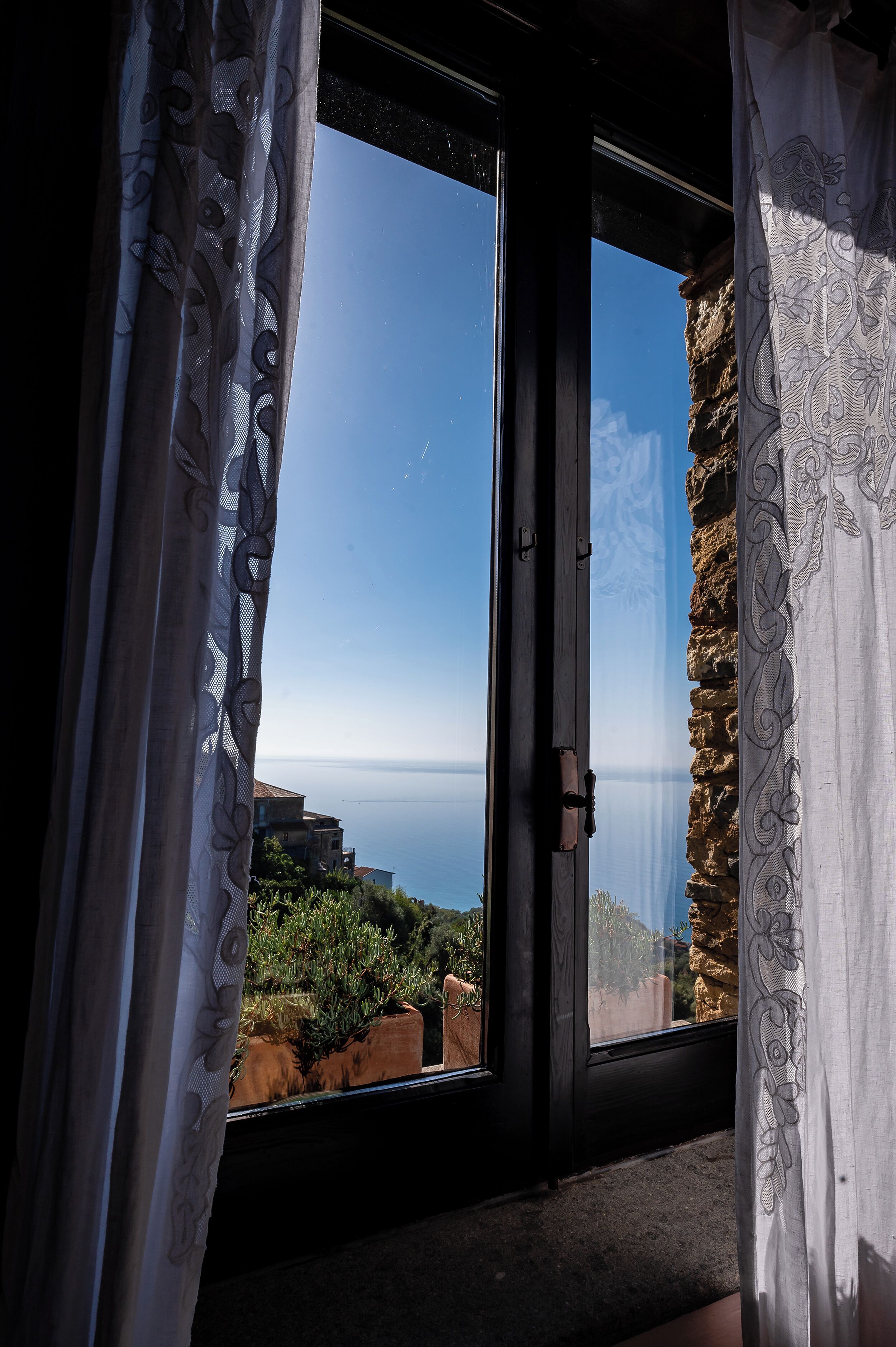 A room with a large glass door leading to a scenic view of the sea and a stone wall.