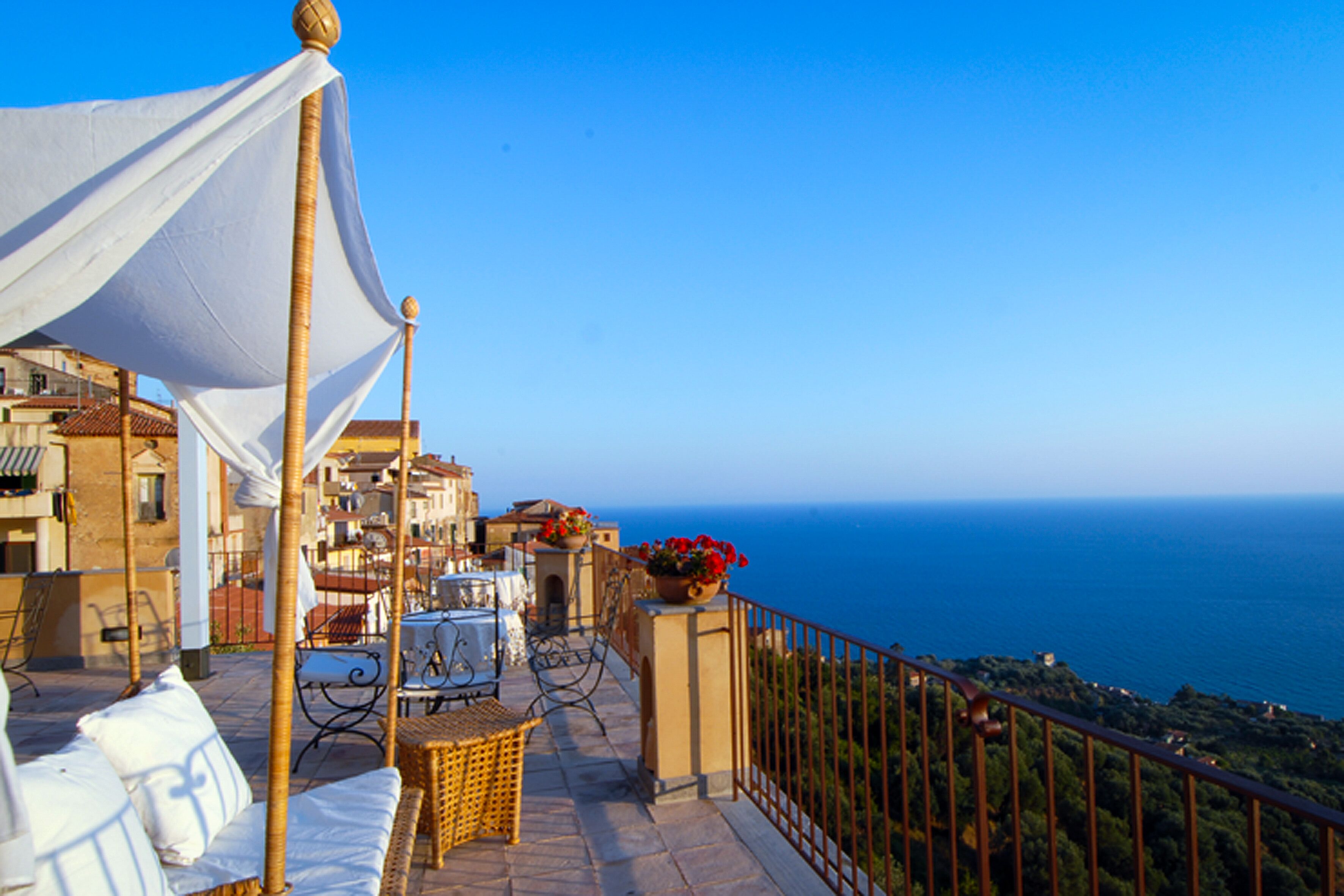 Eine Terrasse mit Korbmöbeln, einem weißen Baldachin und Blick aufs Meer.