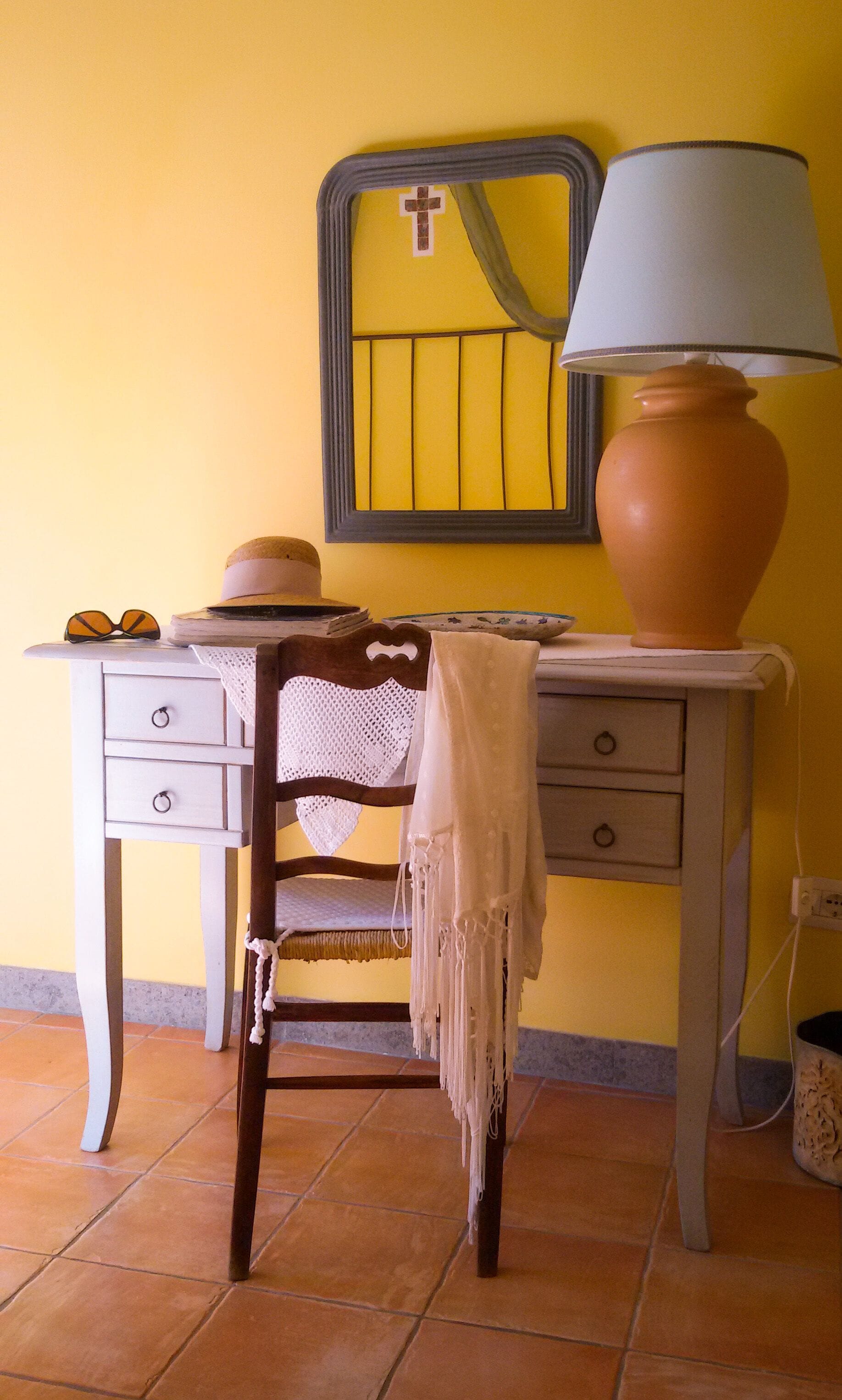 A room with a desk, a chair, a lamp, and a wall-mounted mirror.