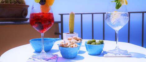 Two drinks on a table with a cactus and bowls of olives and nuts in the background.