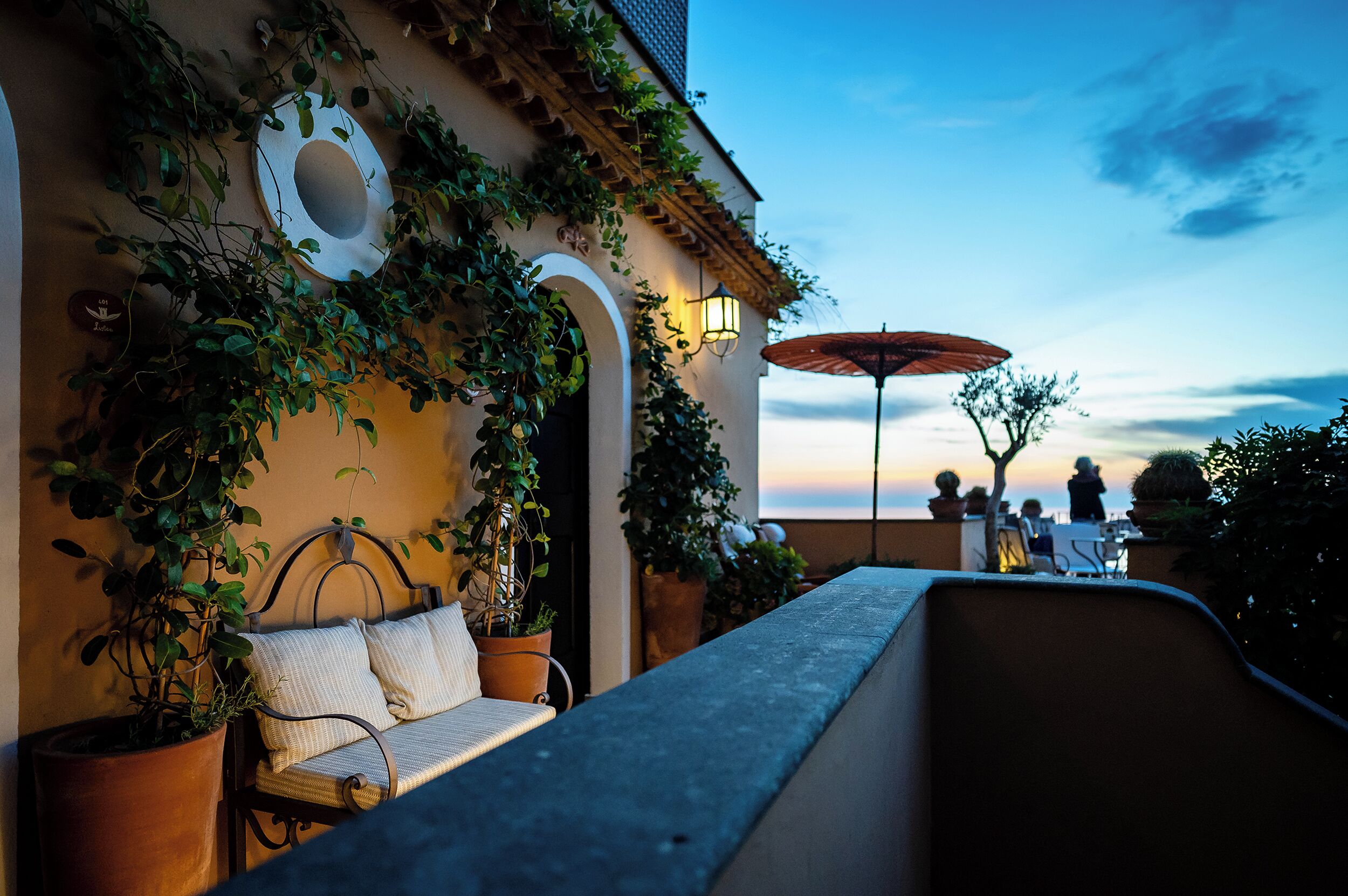 Eine Terrasse mit einer Bank, Kübelpflanzen und einem Tisch.