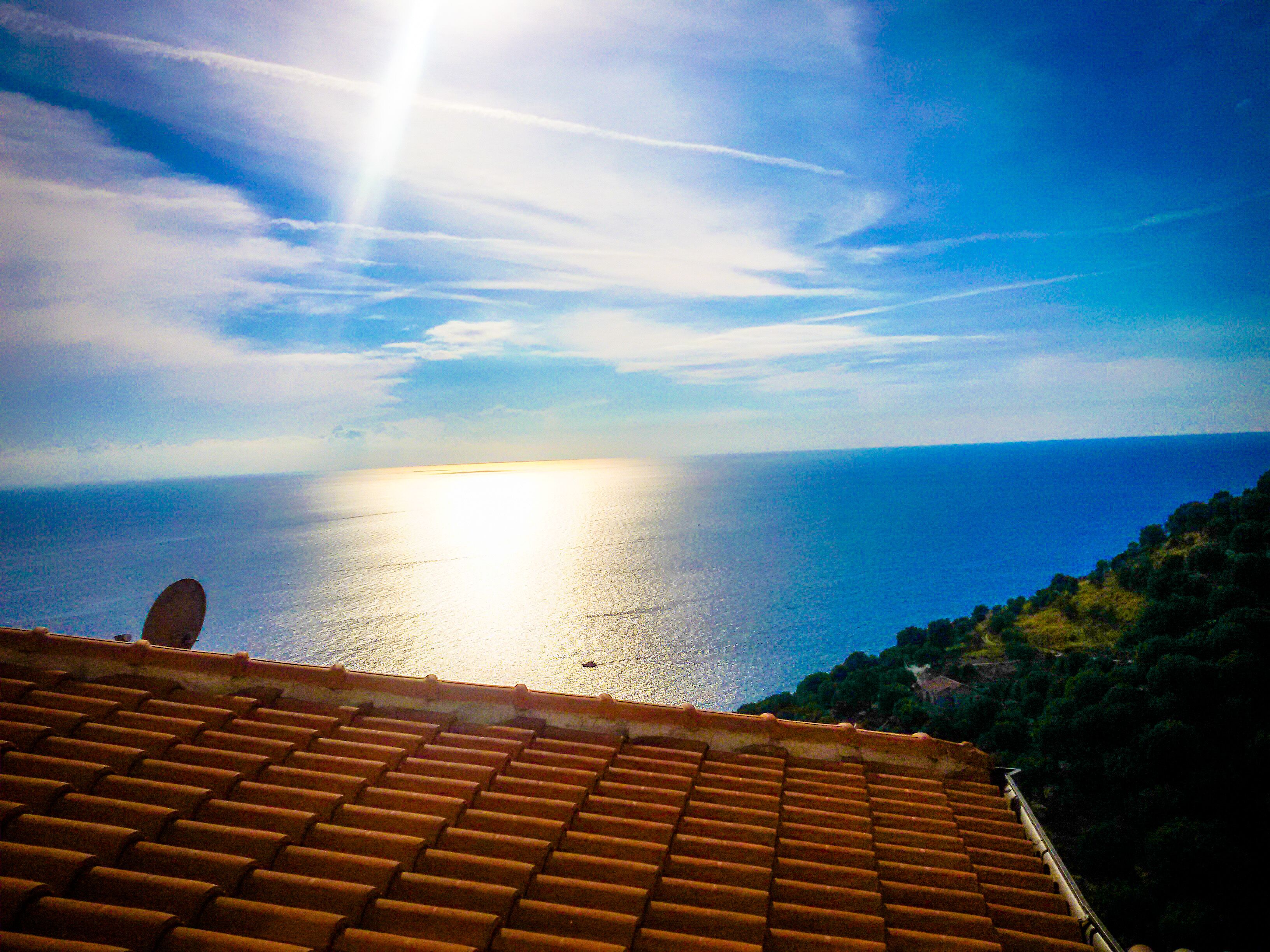 A view of the sea from a tiled roof, with a clear sky and a bright sun.