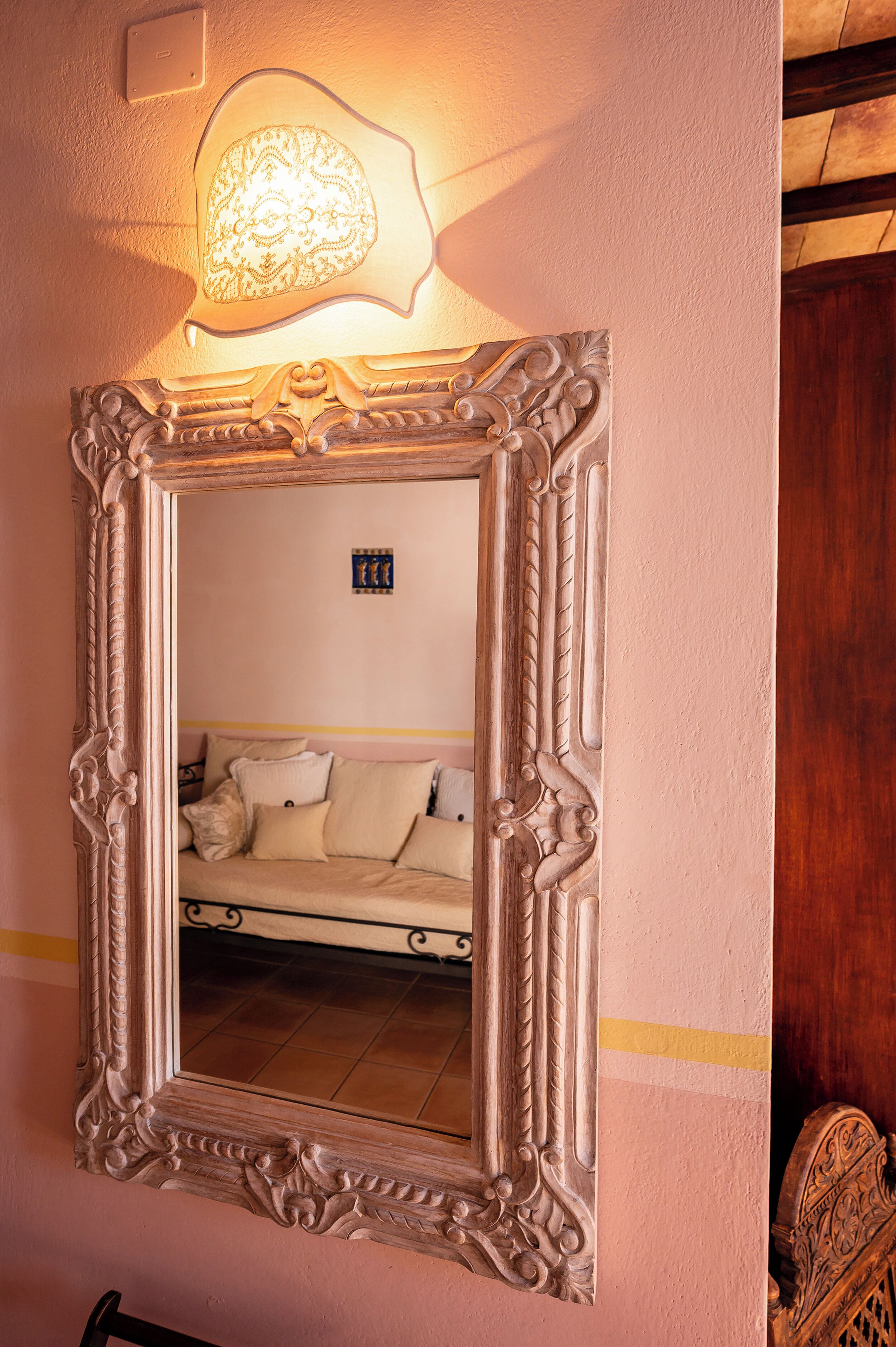 Un espejo con un marco decorado refleja una habitación con un sofá y una lámpara.