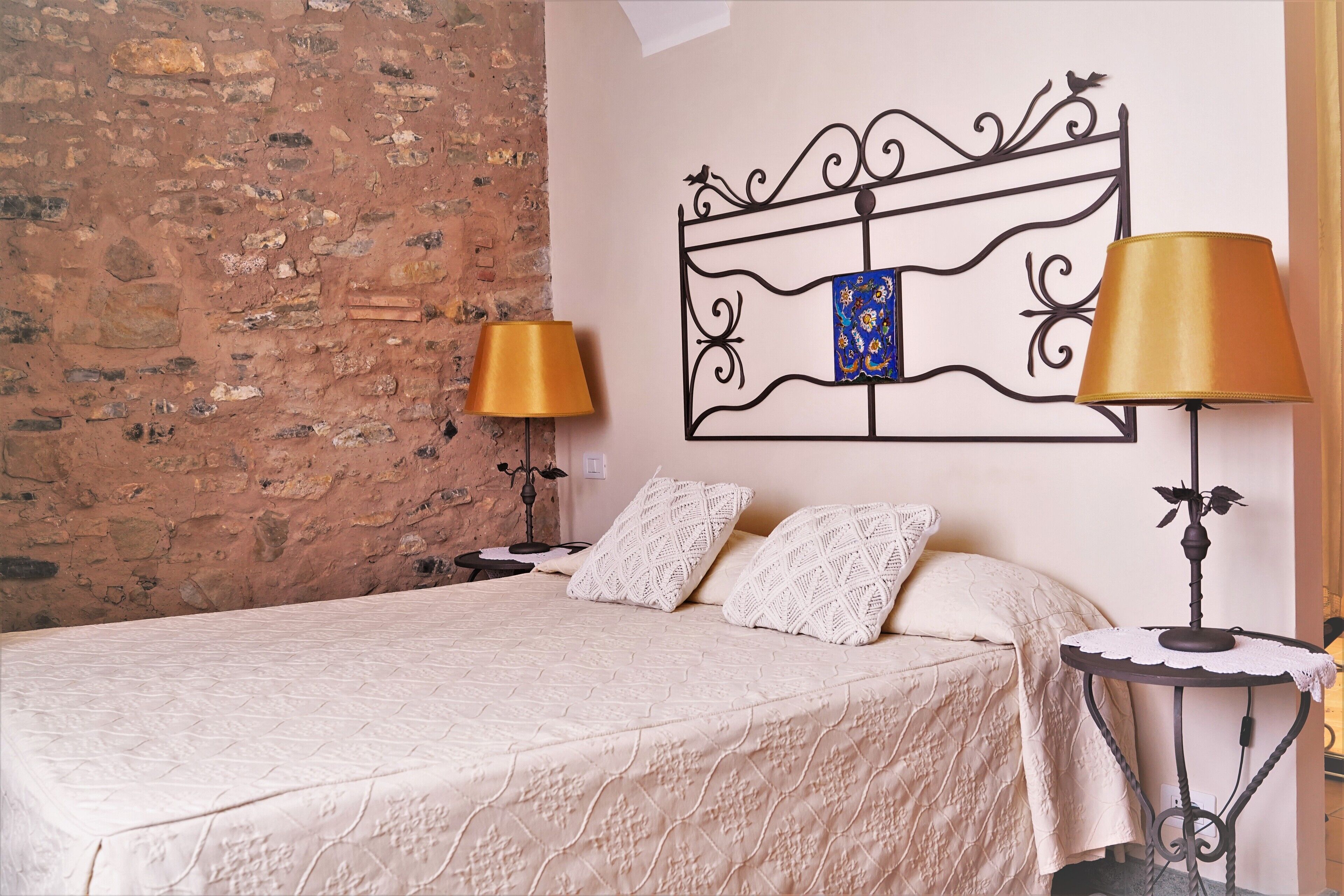 Una cama bien hecha con una colcha estampada, dos lámparas de noche, un cabecero decorativo y una mesita con lámpara.