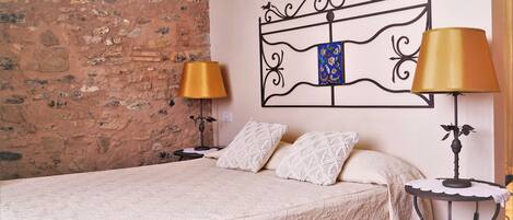 Una cama bien hecha con una colcha estampada, dos lámparas de noche, un cabecero decorativo y una mesita con lámpara.