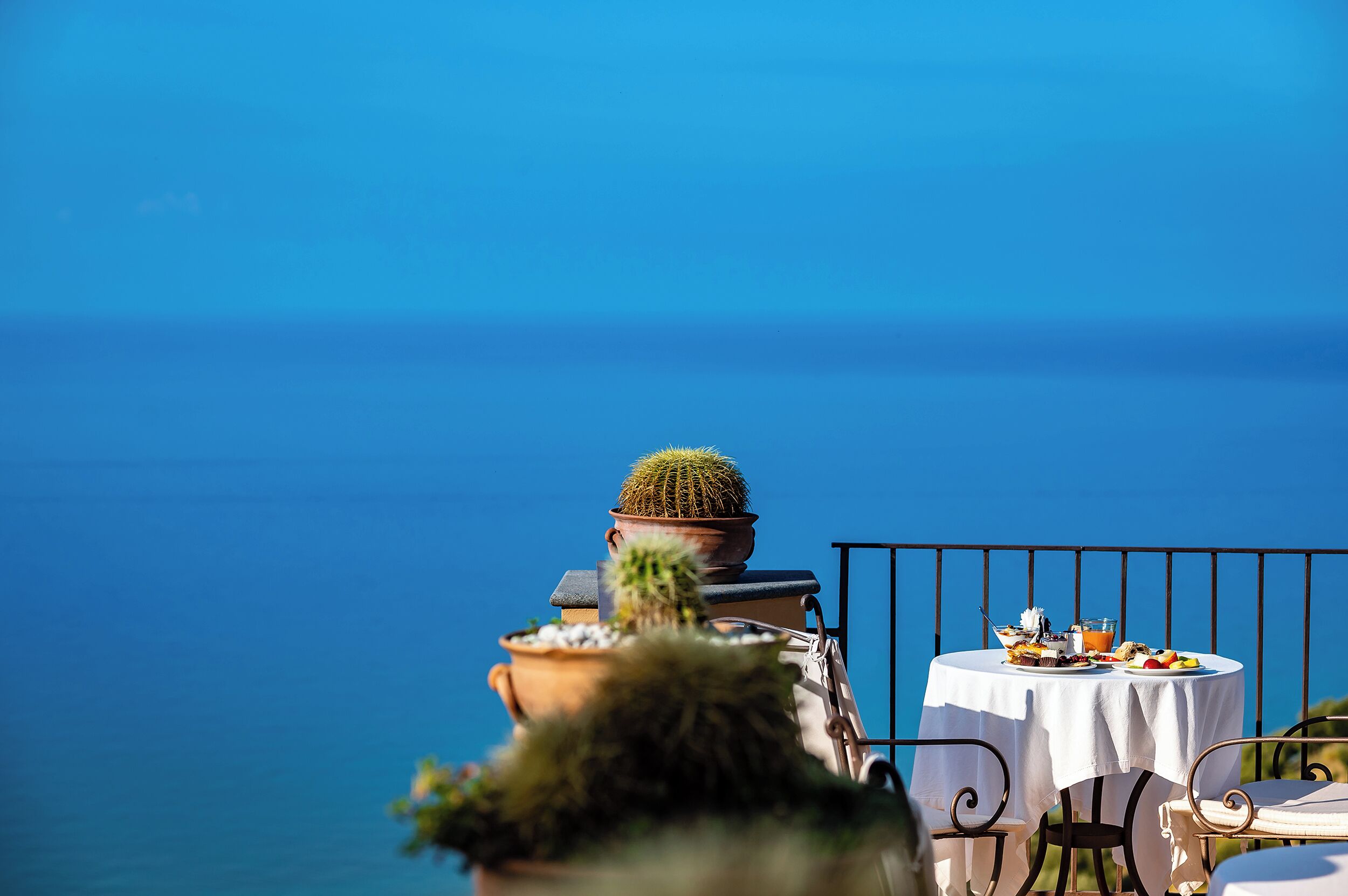 Une table recouverte d’une nappe blanche, dressée avec divers plats, le tout se détachant sur un ciel bleu azur et la mer.